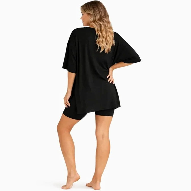 A woman shown from the back wearing a loose black short-sleeve tunic top and matching black shorts against a plain white studio background.