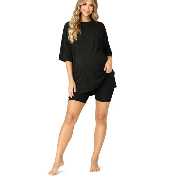 A woman modeling a black oversized short-sleeve top with matching black fitted shorts against a plain white background.