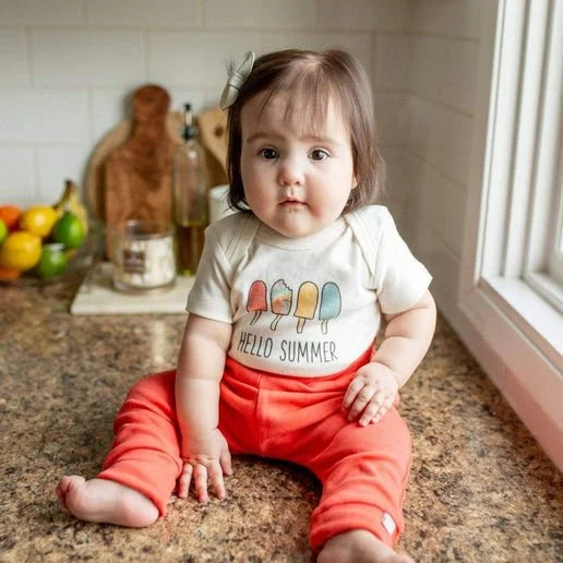 Baby sitting on a kitchen counter wearing a 'Hello Summer' onesie.